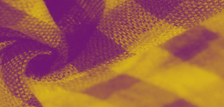 Blur of yellow fabric with checkered patterns and soft creases. The texture is woven intricately, showing the delicate balance between shadow and light, adding depth to the design.の写真素材