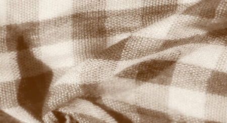 Blur of a beige and brown checkered fabric in a folded, gathered pattern. The material has a soft...