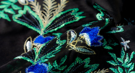 Blur of a midnight blue fabric with ornate, glowing embroidery, capturing delicate floral and leafy...
