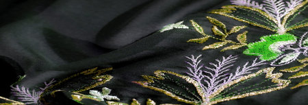 Blur of delicate green and purple embroidery with golden accents on black fabric, emphasizing...
