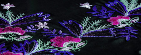 Blur of floral embroidery in vivid pink, green, and purple on a soft black fabric. The intricate...