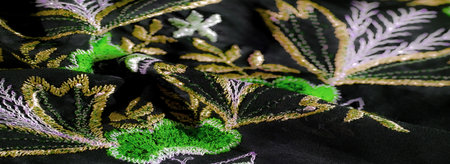Blur of black fabric with green, lavender, and gold embroidery, showing botanical patterns and fine detail, emphasizing the luxurious and ornate texture of the fabric.の写真素材