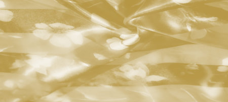 Blur of a soft yellow fabric with delicate folds that reveal faint floral designs. The soft, flowing...