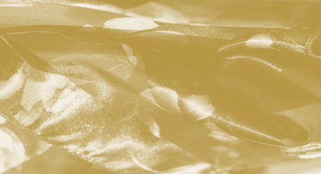 Blur of elegant yellow fabric with soft, light-catching swirls and layered floral designs. The smooth texture and transparency offer a delicate charm, blending light and texture harmoniously.の写真素材