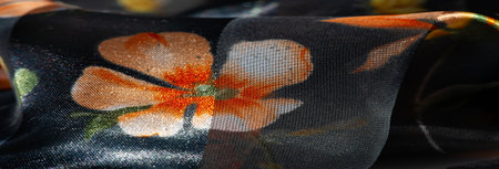 Blur of a glossy sheer fabric adorned with orange and yellow floral elements, blending transparency and texture. Soft lighting enhances its luxurious appeal.の写真素材