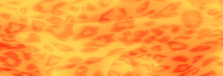 Blur of bright yellow and red patterned fabric in closeup, showing the mesh-like texture and vibrant abstract shapes. The soft folds give a dynamic and warm visual appeal.の写真素材