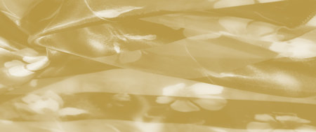 Blur of light yellow fabric with delicate folds and faint floral patterns. The soft texture and smooth appearance create a serene and elegant background, enhanced by subtle light reflections.の写真素材