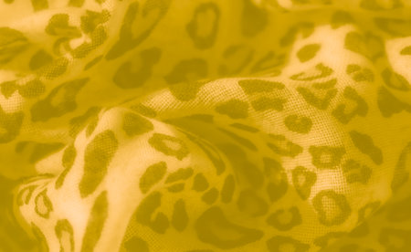 Blur of textured yellow fabric featuring leopard-inspired patterns, capturing smooth, gentle folds that bring warmth and a sense of movement to the design.の写真素材