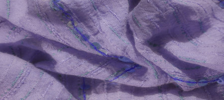 Blurred view of a light purple fabric decorated with green and blue stitching lines and sequins. The soft texture and subtle folds add dimension to the textile's appearance.の写真素材