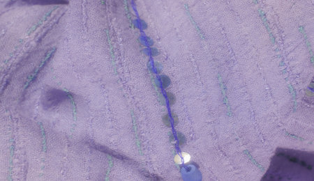 Blurred lavender textile with green and blue embroidered lines and a scattering of sequins. The gentle drapes and shimmering sequins create a refined, luxurious fabric texture.の写真素材