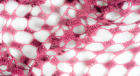 Blurred image of pink lace fabric, showing an intricate open weave pattern that adds texture and...