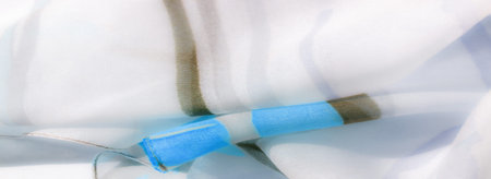 Blur of delicate fabric with hints of blue and beige, creating a soft, flowing effect. The...