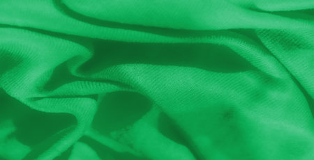 Blur of a detailed close-up of green fabric folds, showing soft textures and subtle light play, ideal for backgrounds and textile-focused visual designs.の写真素材