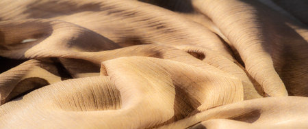 Blur - Soft folds of golden-brown fabric create a gentle, flowing texture. Light and shadow dance across the surface, accentuating the fabric's natural sheen and subtle transparency.の写真素材