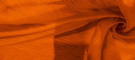 Blurred view of orange fabric with flowing folds and delicate shadowing. The soft texture and warm tones create a cozy, inviting look, perfect for textile detail shots.の写真素材