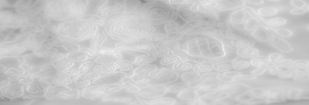 Blur of intricate white lace fabric with delicate floral and spiral patterns, showing subtle textures and fine detailing in a soft, elegant style.の写真素材