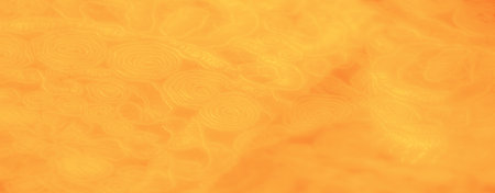 Blur. The warm yellow fabric with intricate swirl and floral patterns appears illuminated by a soft glow, highlighting its delicate texture and adding a vibrant appeal to the textile.の写真素材