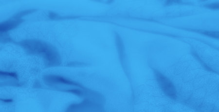 Blur of a flowing, textured blue fabric with intricate folds that create depth and a soft visual appeal. The fabric texture adds dimension to the smooth blue hues.の写真素材