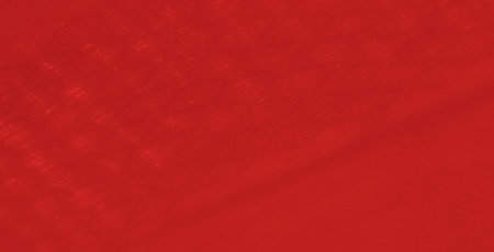 Blur of a deep red fabric with flowing folds and intricate details in the weave. This close-up...