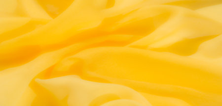 Blur - Delicate folds of soft yellow fabric cascade in gentle swirls, capturing light and creating a warm, inviting texture. Perfect for backgrounds and textile themes.の写真素材