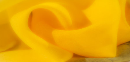 Blur - Elegant folds of yellow fabric arranged in a mesmerizing swirl pattern. This vibrant yellow with soft texture provides a warm and inviting feel, perfect for creative backgrounds.の写真素材