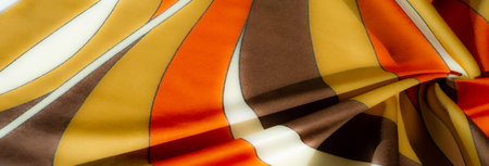 Blurred orange, yellow, and brown striped fabric with soft folds and a smooth satin-like texture....