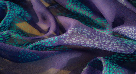 Blurred fabric with intricate teal and turquoise dot patterns over a purple base. The soft, fluid...