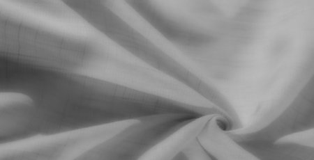 Blurred folds of soft grayscale fabric create an intricate, spiraling texture. The interplay of light and shadows highlights the smooth, delicate material.の写真素材