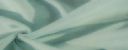 Blur of soft pastel green fabric in intricate folds, with faint grid patterns highlighted by soft...