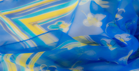 Blur The image captures a vibrant blue fabric with delicate floral patterns featuring yellow and white blossoms, creating a soft and airy texture with light ripples.の写真素材