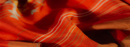 Blurred image highlighting bright orange fabric with soft, flowing folds. Subtle stripes and vibrant floral patterns add texture and aesthetic depth.の写真素材