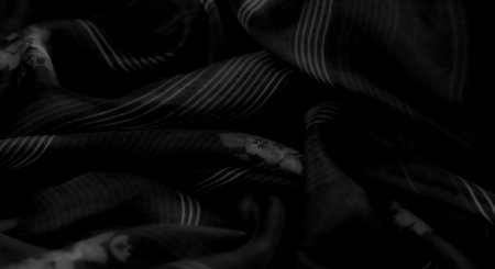 Blurred folds of dark textured fabric featuring soft stripes and a floral design create an elegant...