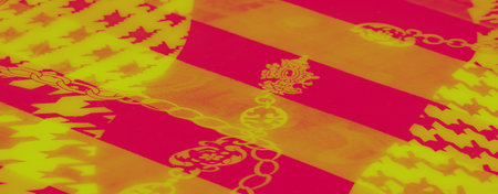 Blur of a vibrant yellow and red patterned fabric featuring ornate floral and chain motifs, with a bold geometric houndstooth background, exuding warmth and energy.の写真素材