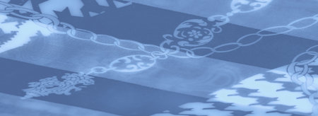 Blurred folds of smooth blue fabric adorned with symmetrical geometric and chain patterns, reflecting intricate details and a modern artistic touch.の写真素材