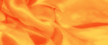 Blur of silky orange fabric draped in delicate folds, radiating a golden glow with subtle highlights. The texture is smooth, giving a luxurious appearance.の写真素材