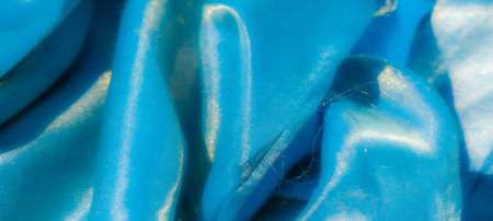 Blurred folds of smooth blue satin fabric shimmer under light, creating a mesmerizing play of glossy textures and vibrant hues that evoke luxury and sophistication.の写真素材