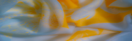 Blurred folds of soft yellow and blue fabric cascade gently, featuring abstract patterns that enhance its artistic and airy texture, glowing with soft light.の写真素材