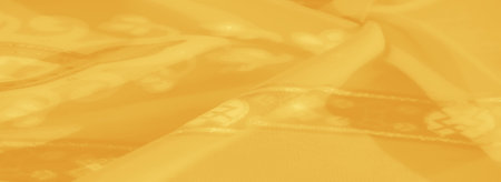 Blurred close-up of yellow fabric with intricate floral and geometric details, highlighting the shimmering texture and vibrant hues for elegant textile themes.の写真素材