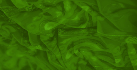 Blur of a green fabric featuring ornate patterns with floral motifs and gentle shimmering accents, creating an artistic and elegant visual effect.の写真素材