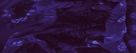 Blurred image showing a purple textured fabric with intricate floral and abstract motifs,...