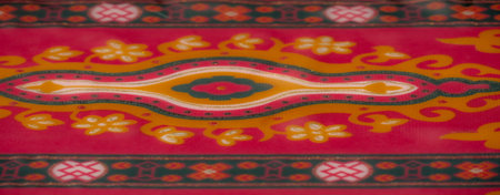 Blurred vibrant red and orange textile featuring symmetrical floral patterns and delicate golden...