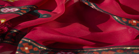 Blur effect enhances the intricate red fabric with bold patterns of orange floral designs and dark...