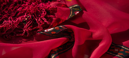 Blurred intricate red and orange fabric featuring floral and abstract patterns with fine golden...