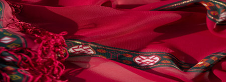 Blurred rich red fabric highlighted with tassels and intricate gold and geometric accents. The...