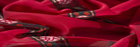 Blurred close-up of vibrant fabric with red, orange, and dark green hues, featuring intricate floral...