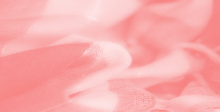 Blur of delicate coral-pink fabric with shimmering textures and frayed edges, creating a soft and dynamic abstract composition perfect for backgrounds and designs.の写真素材
