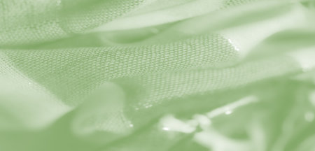 Blurred soft green fabric with layered folds and faintly visible threads, offering a light and airy texture for a subtle abstract background design.の写真素材