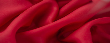 Blurred close-up view of a red fabric texture with delicate folds and a smooth finish, offering a modern and vibrant aesthetic suitable for various creative applications.の写真素材