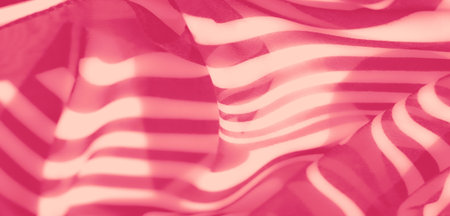 Blur of delicate pink fabric with wavy, semi-transparent layers creating an abstract pattern of light and shadow, adding a soft and elegant feel.の写真素材