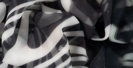 Blur of smooth black and white fabric featuring dynamic swirls and abstract patterns, providing a...